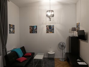 Ein modernes Wohnzimmer mit einem schwarzen Sofa, roten Kissen, einem weißen Couchtisch, einer schwarzen TV-Konsole und einer Chandelieber.