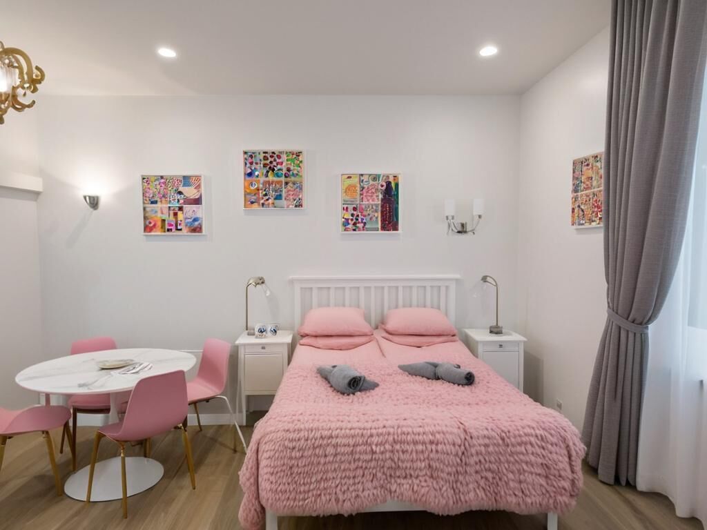 A bedroom with a bed, a desk, a chair, a round table, and artwork on the walls.