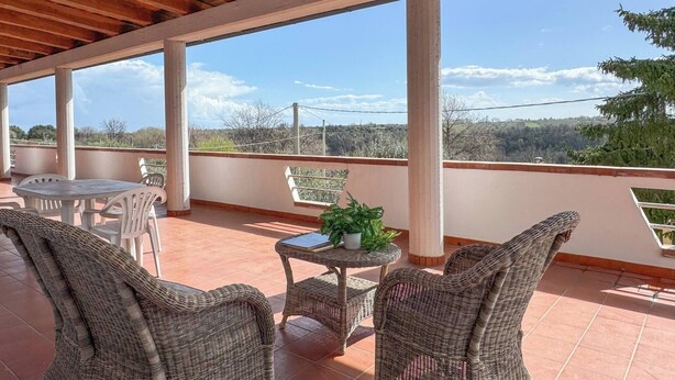 Un patio techado al aire libre con mobiliario de mimbre, una mesa con una planta y vistas al paisaje.