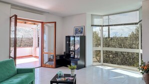 Una sala de estar moderna con un sofá verde, un mueble de entretenimiento negro y un ventanal con vistas a árboles.