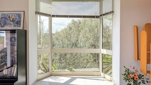 Habitación de esquina con un ventanal grande, un cuadro en la pared y un jarrón con flores.