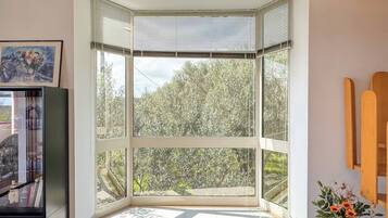 Ein Eckzimmer mit großem Fenster, einem gerahmten Bild an der Wand und einer Vase mit Blumen.