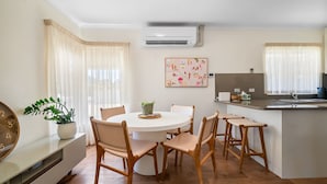 A modern kitchen with a round dining table, wooden chairs, and a built-in island with a sink.