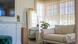 A living room with a sofa, a television, a fireplace, and a large window with sheer curtains.
