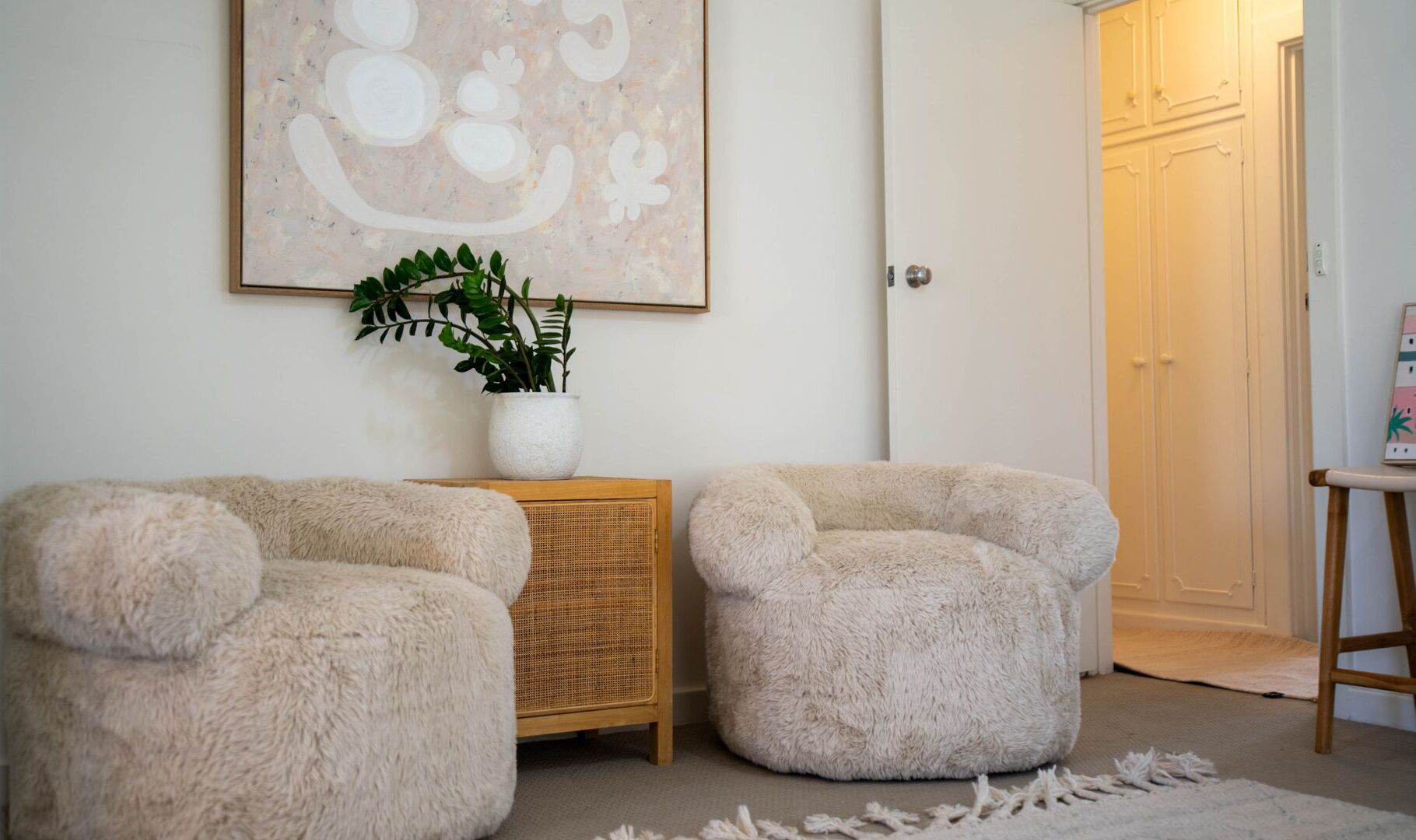 A room with two plush armchairs, a wicker side table with a plant, and a framed artwork on the wall.