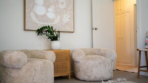 A room with two plush armchairs, a wicker side table with a plant, and a framed artwork on the wall.