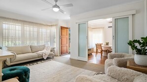 A spacious living room with a sofa, a dining table, and a ceiling fan.