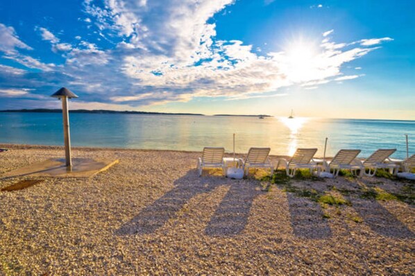A pebbled beach with sun loungers and a lifeguard tower.