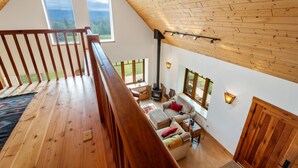 A loft-style room with a wooden ceiling, large windows, a fireplace, and a cozy seating area.