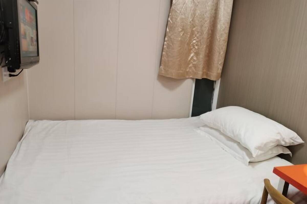 A single bed with white bedding, a wooden chair, and a small orange table.