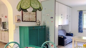 A room with a dining table, chairs, a bowl of fruit, a green cabinet, a bed, and a wardrobe. - Villa Le Cicale - Salento (Morciano di Leuca)