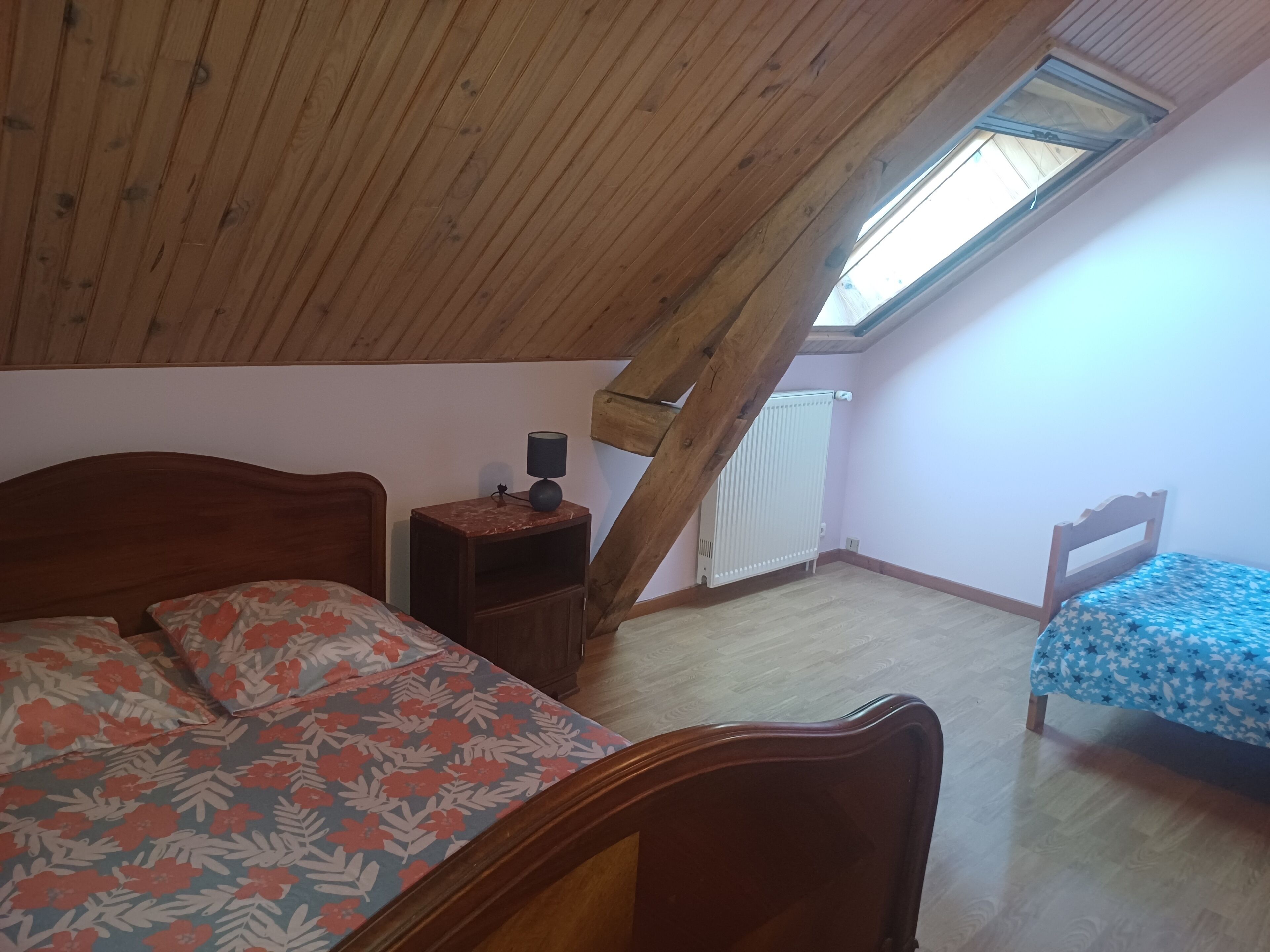 Un dormitorio con techo inclinado, una cama de madera, una mesita de noche con lámpara y un radiador.