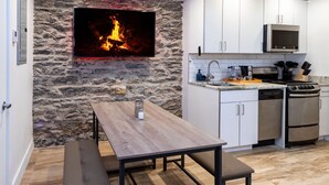 Una cocina moderna con armarios blancos, una pared de piedra, un televisor de pantalla plana y una mesa de comedor de madera.