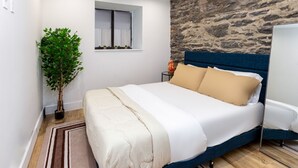 Un dormitorio con cama, planta en maceta, ventana y pared de piedra.