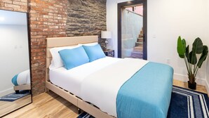 Un dormitorio con pared de ladrillo, una cama con ropa de cama azul, una planta en maceta y vistas a una escalera.