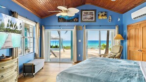Ein Schlafzimmer mit einem großen Bett, einem Deckenventilator, einer Bank und Blick auf den Strand durch eine Schiebetür.