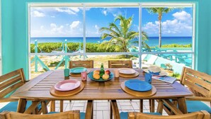 Ein Essbereich mit Tisch für vier Personen, mit Blick auf einen Strand, Palmen und das Meer.