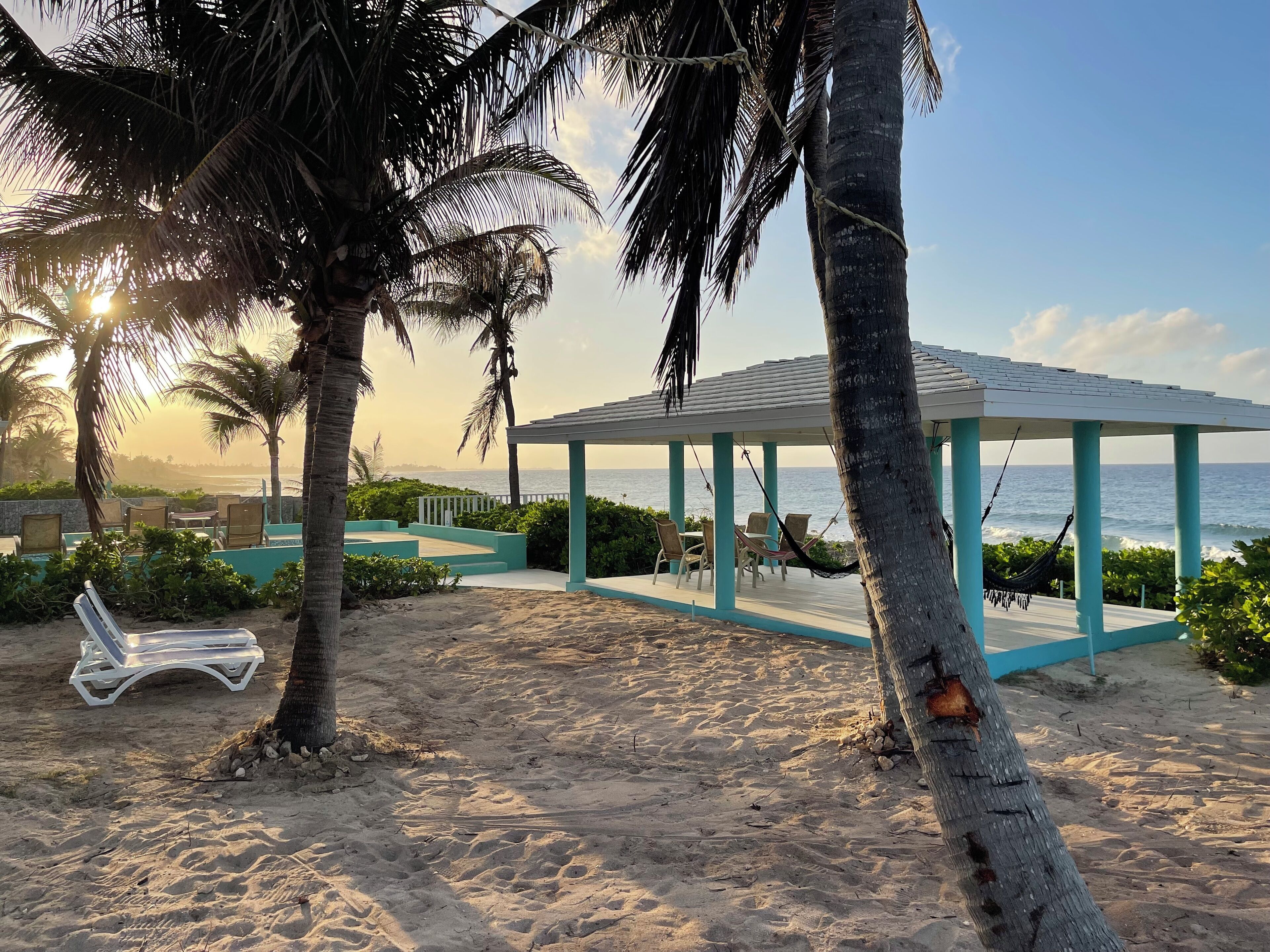 A beachside area with a gazebo, lounge chairs, and palm trees.