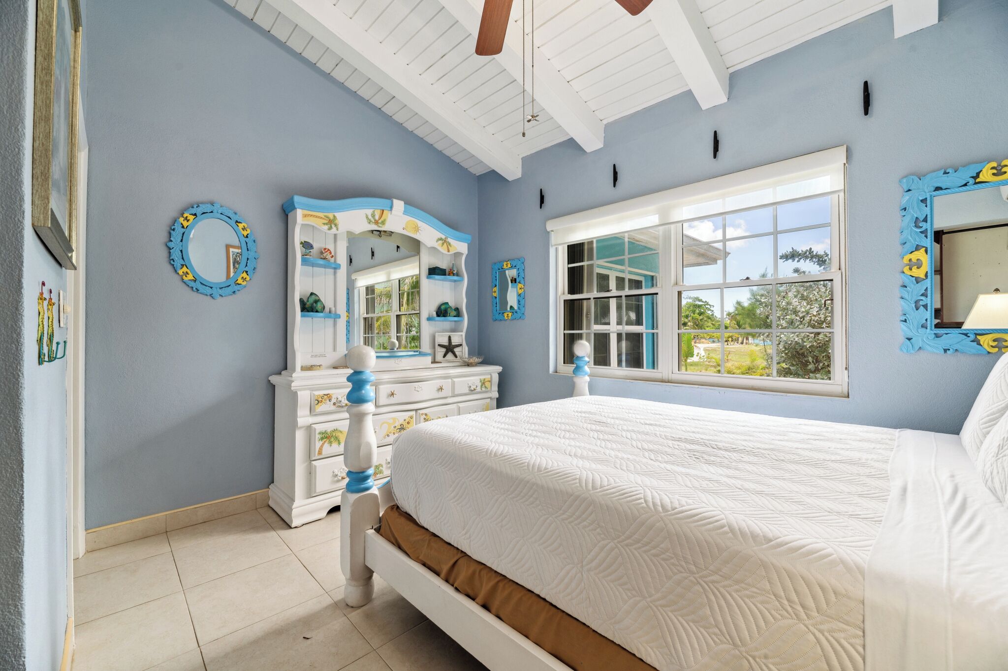 A bedroom with a large bed, a dresser, a mirror, and a window with a view.