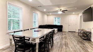 A spacious living area with a dining table, chairs, a black sofa, and a ceiling fan. - Beach House By The Bay, 9 Car Parking, Linen Included (Lower Township)