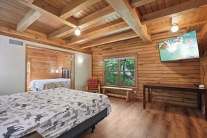 A wooden cabin room with a bed, a bench, a table, and a TV mounted on the wall.