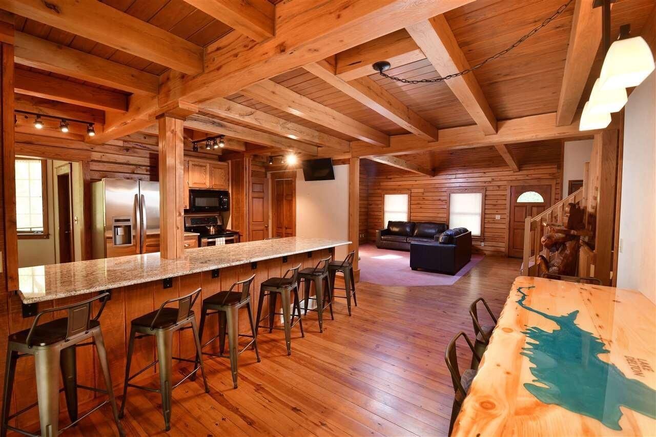 A spacious kitchen with wooden beams, a long bar with stools, and a dining table with chairs.