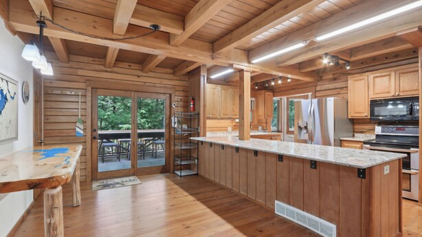 A wooden cabin interior with a kitchen area, wooden beams, and a large window. - Charming 7-bedroom lodge with AC, WiFi in awesome Lake Delton Wisconsin Dells (Baraboo)
