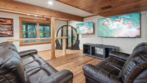 A living room with leather sofas, a wooden ceiling, a large window, and a TV mounted on the wall. - Charming 7-bedroom lodge with AC, WiFi in awesome Lake Delton Wisconsin Dells (Baraboo)