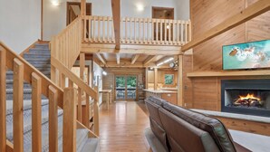 A wooden staircase leading to a balcony, a fireplace with a TV, and a seating area with a view of the outdoors. - Charming 7-bedroom lodge with AC, WiFi in awesome Lake Delton Wisconsin Dells (Baraboo)