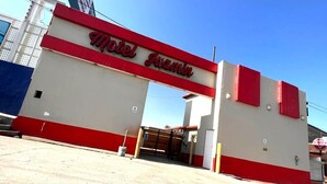 Un hôtel appelé « Motel Quimino », avec une façade rouge et blanche, une entrée fermée par un portail et un ciel dégagé en arrière-plan.