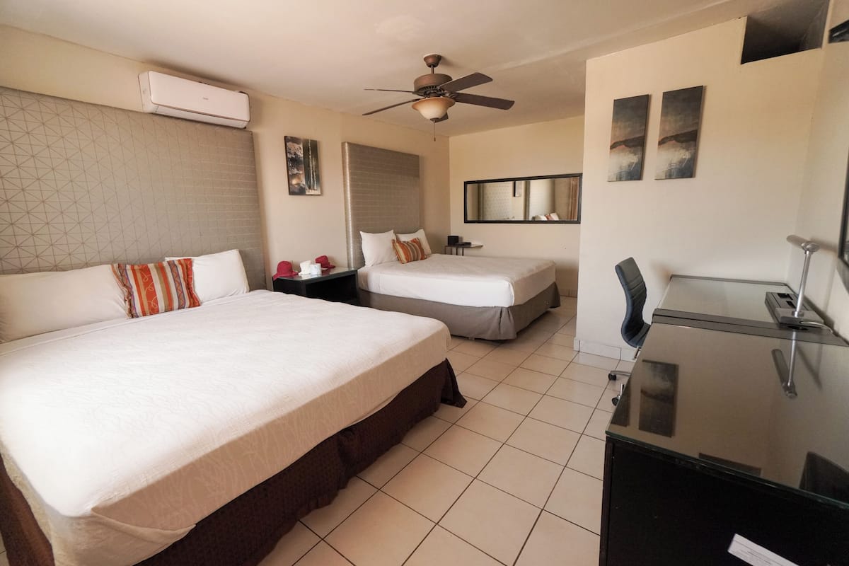 A hotel room with two beds, a desk, a chair, a ceiling fan, and a large mirror.