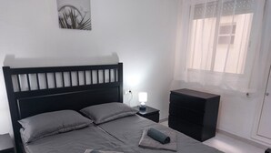A neatly made bed with two pillows and two folded towels, a bedside table with a lamp, and a small nightstand. - 2-bedroom apartment - close to beaches and center (Torrevieja)