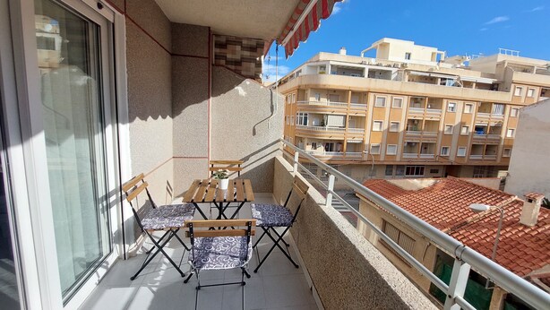 A balcony with a table and chairs, a potted plant, and a view of neighboring buildings. - 2-bedroom apartment - close to beaches and center (Torrevieja)