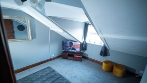 A room with a sloped ceiling, a television on a stand, a mirror, and a window with curtains.