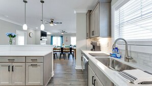 Une cuisine moderne avec un îlot central, un coin repas avec des chaises et une grande fenêtre équipée de stores.