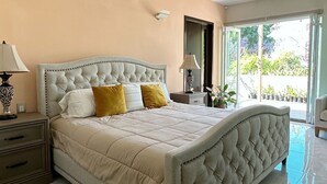 Un dormitorio amplio con una cama grande, una mesita de noche, una lámpara y vistas al exterior a través de un ventanal.