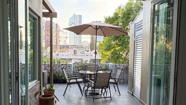 Un patio abierto con una mesa, sillas, una planta en maceta y vistas de la ciudad.