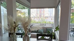 Un comedor moderno con una mesa de madera oscura, jarrones blancos con plumas de pampa y vistas a un paisaje urbano a través de grandes ventanales.
