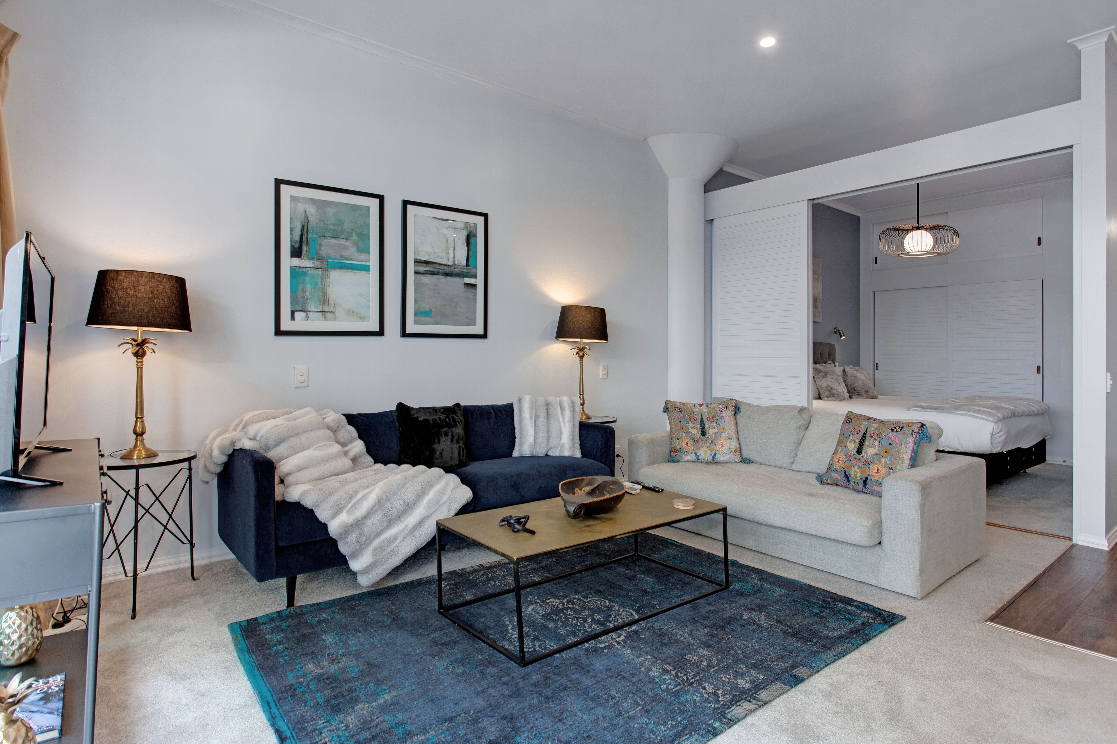 A modern living room with a dark blue sofa, a white sofa, and a coffee table. There are two lamps on either side of the room, and a painting on the wall.