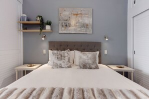 A bedroom with a tufted headboard, two bedside tables, a large abstract painting, and a grey wall.