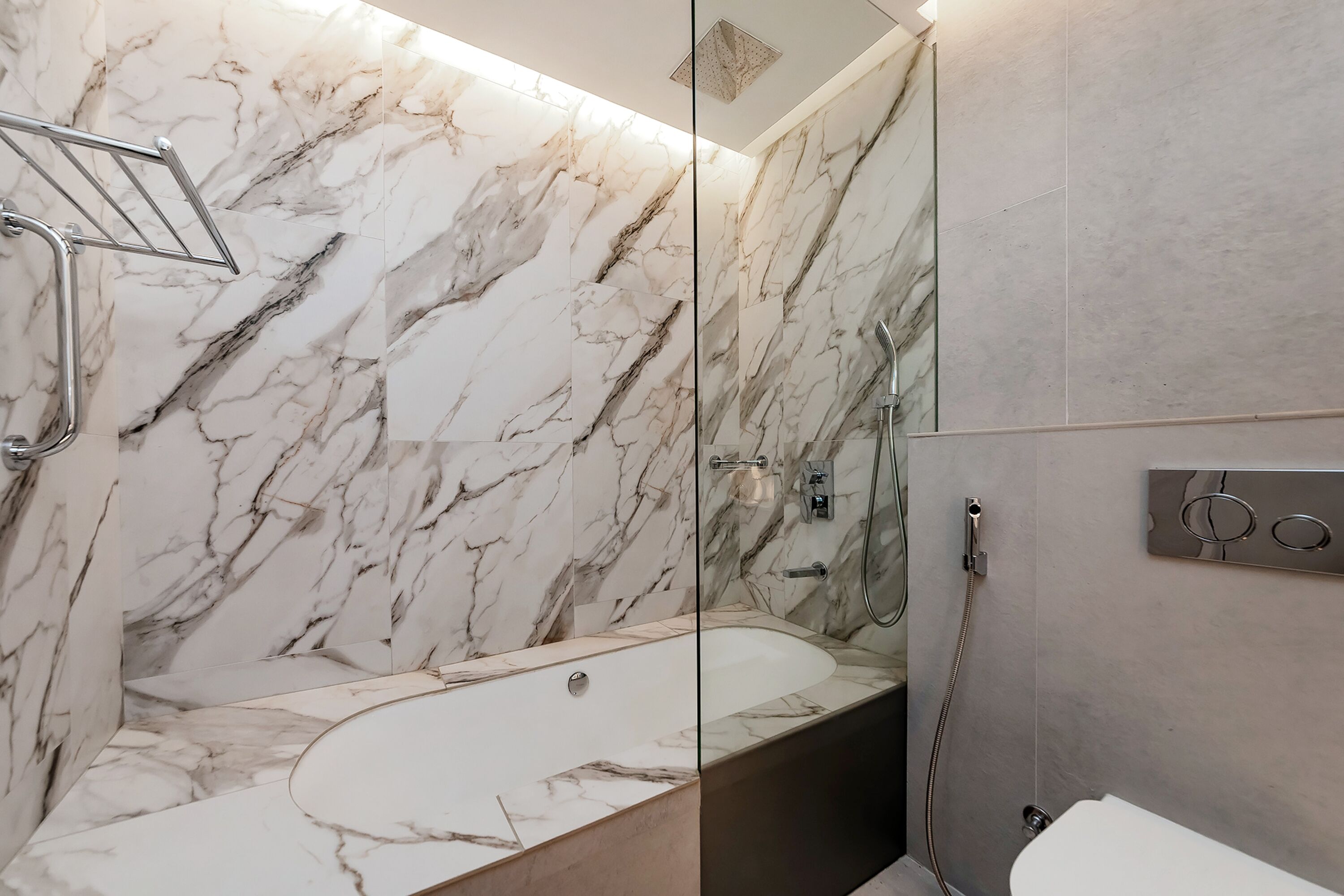 A modern bathroom with a marble wall, a freestanding bathtub, and a glass-enclosed shower area.