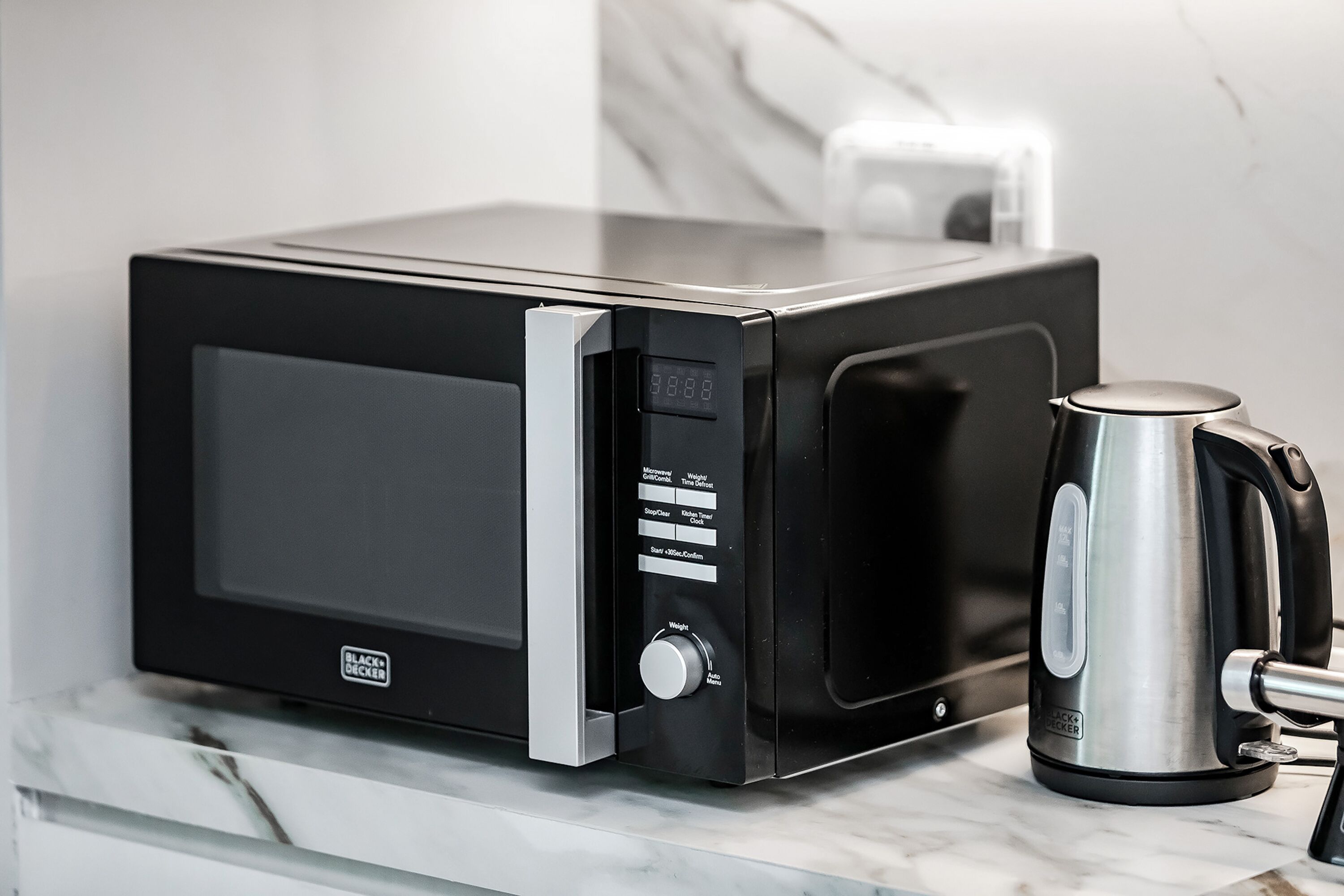 Een moderne keuken met een zwarte magnetron en een roestvrijstalen waterkoker op een marmeren aanrecht.