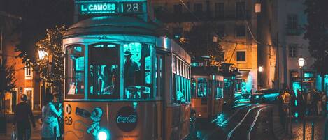 Un tram avec une plaque indiquant « L. CAMOES 28 » roule dans une rue de la ville, de nuit.