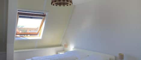 A bedroom with a bed, a window, a bedside table, and a lamp.