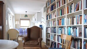 A library with bookshelves, a brown leather armchair, a wooden chair, and a table. - Apartment With Dunes View of Petten (Petten)