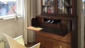 A room with a large wooden cabinet with glass doors, a white chair, and a window with curtains. - Apartment With Dunes View of Petten (Petten)