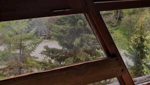 Une vue à travers une fenêtre à cadre en bois, donnant sur un paysage montagneux avec des arbres et des sommets enneigés.