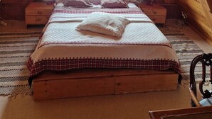 Une chambre mansardée chaleureuse, avec un plafond en pente, une grande fenêtre avec des rideaux, un lit avec des oreillers et une table de chevet en bois.