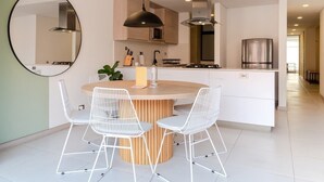 A modern kitchen with white cabinetry, a round wooden island with two white wire chairs, a hanging pendant light, and a large mirror on the wall. - NOK Bright 3BR with terrace in Laureles Medellin (Medellín)