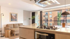 A modern kitchen with a built-in oven, a dining area with a sofa, and a large window offering a view of the city. - NOK Bright 3BR with terrace in Laureles Medellin (Medellín)